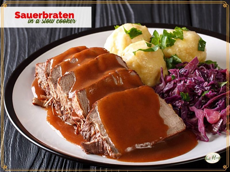 sliced sauerbraten on a plate with gravy, potatoes and red cabbage