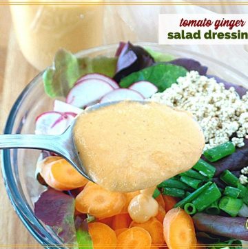 salad dressing on a spoon over a salad with text overlay "creamy tomato ginger salad dressing"