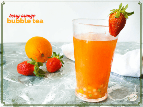 glass of berry orange boba tea with strawberries and orange in background