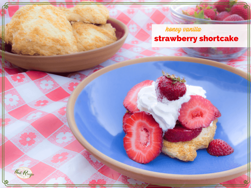 strawberry shortcake on a blue plate with strawberries and shortcake in the background and text overlay "Honey Vanilla Strawberry Shortcake"