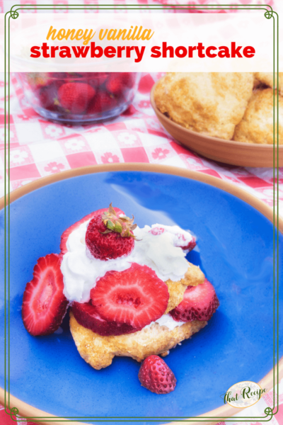 strawberry shortcake on a blue plate with strawberries and shortcake in the background and text overlay "Honey Vanilla Strawberry Shortcake"