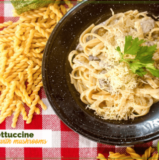 fettucine and mushrooms on a black plate on a red and white checked table cloth.