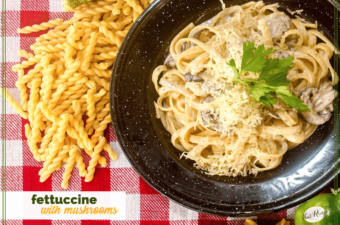 fettucine and mushrooms on a black plate on a red and white checked table cloth.