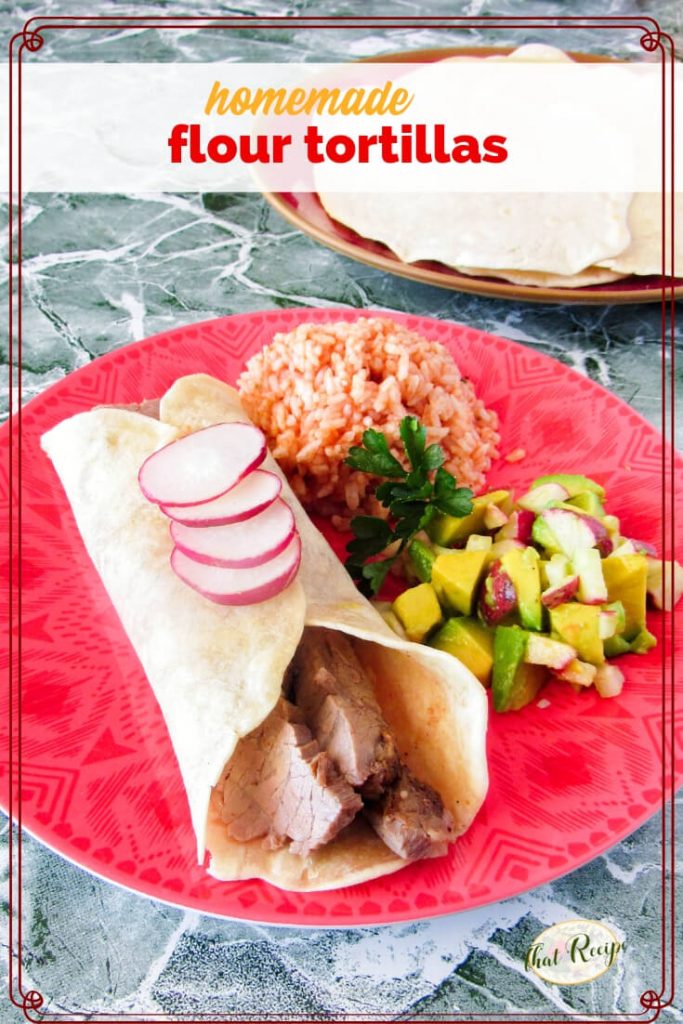 steak burrito on a plate with Mexican rice, avocado salsa and flour tortillas in the background with text overlay "homemade flour tortillas"