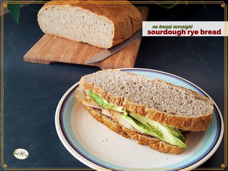turkey and avocado sandwich on rye bread with loaf of ry bread in the background and text overlay "sourdough rye bread"