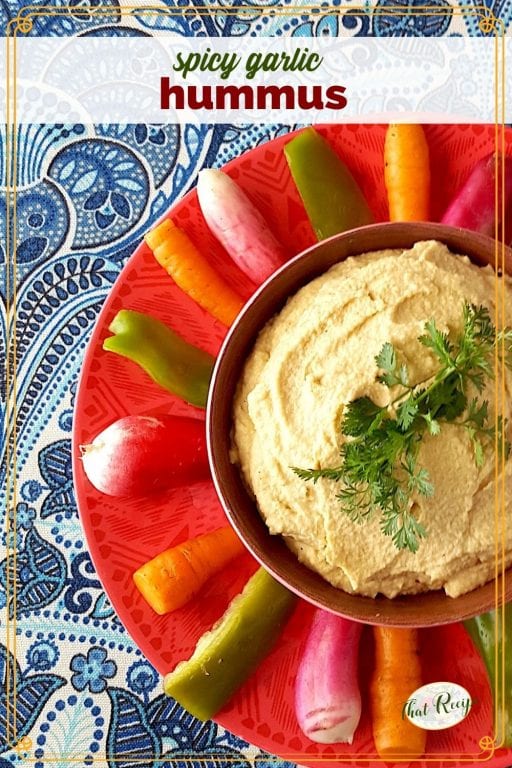 bowl of hummus with vegetables around it on a plate and text overlay "spicy garlic hummmus"