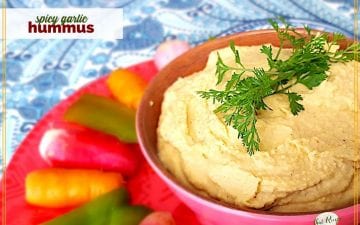 bowl of humus with vegetables around it on a plate and text overlay "spicy garlic hummmus"
