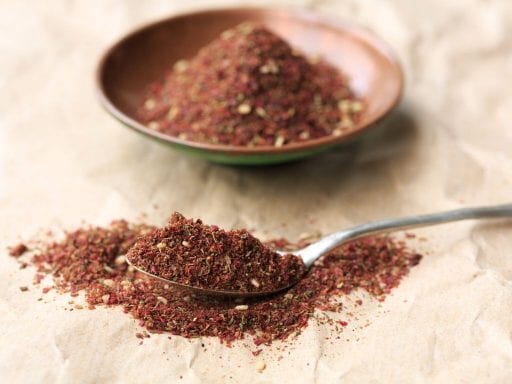 Za'atar spice mix in a small bowl and spilled on a table and spoon