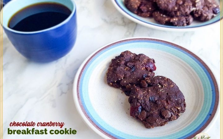 two chocolate cookies on a plate with a cup of coffee next to it and text overlay "Chocolate cranberry breakfast cookies"