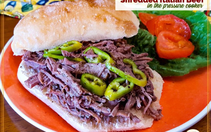 shredded beef sandwich on a plate with lettuce, tomatoes and peppers with text overlay "Shredded Italian Beef in the pressure cooker"