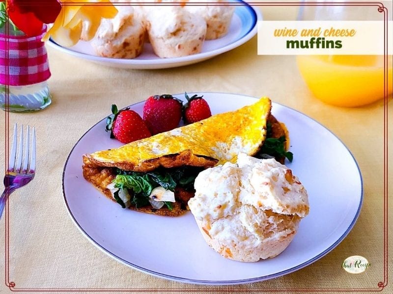 muffin on a plate with spinach omelet and fresh fruit and text overlay "wine and cheese muffins"