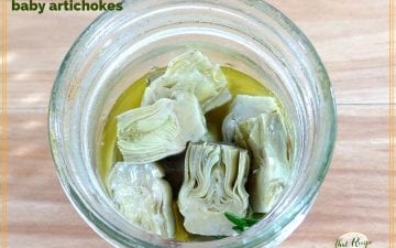 baby artichokes in a jar with text overlay "marinated baby artichokes"