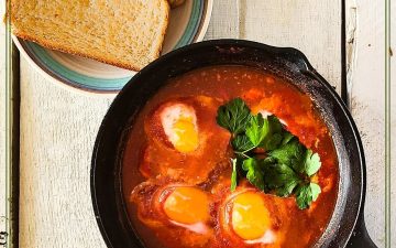 cast iron skillet with eggs in tomato sauce and text overlay "eggs in purgatory"