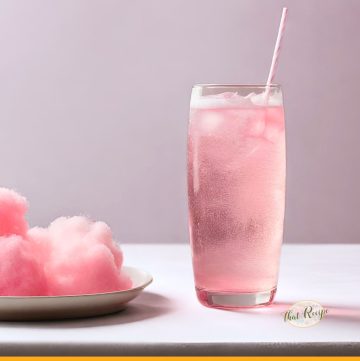 glass of sparkling pink drink with a plate of cotton candy