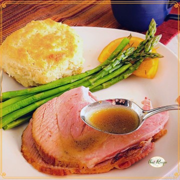 spoon of red eye gravy over plate of ham, asparagus and biscuit.