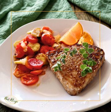 swordfish steak on a plate with vegetables and citrus fruit