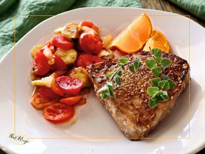 swordfish steak on a plate with vegetables and citrus fruit