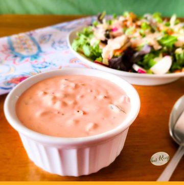 cup of thousand island dressing with a salad in background