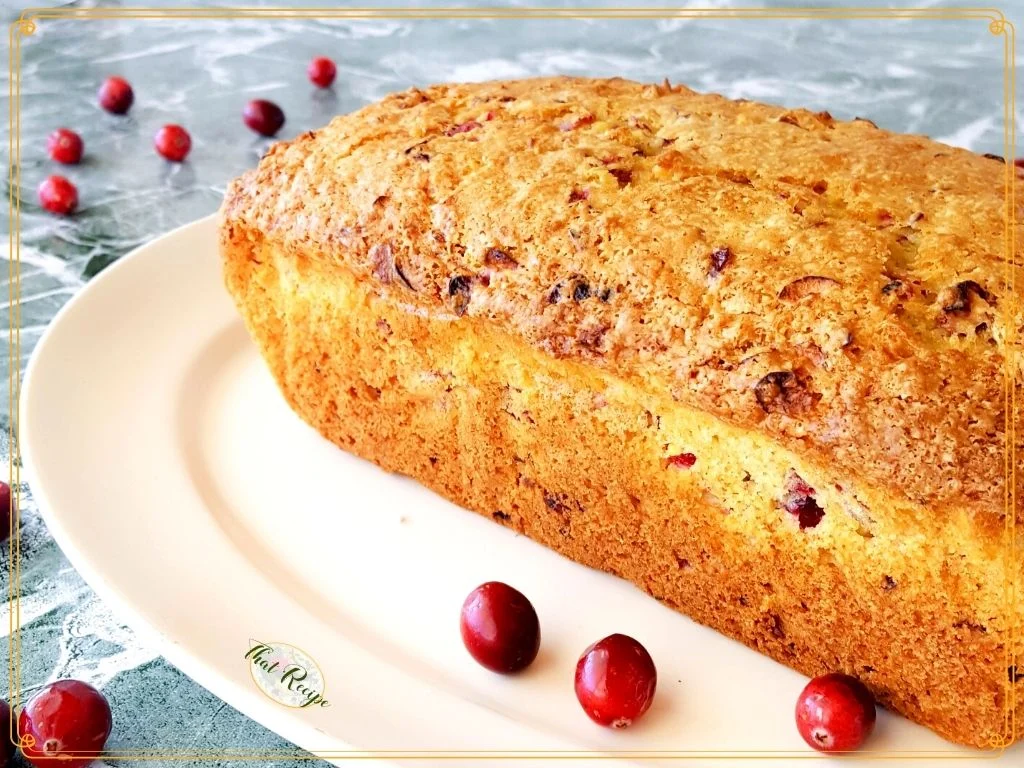 loaf of quick bread on a plate surrounded by cranberries with text overlay "Cranberry whole orange bread".