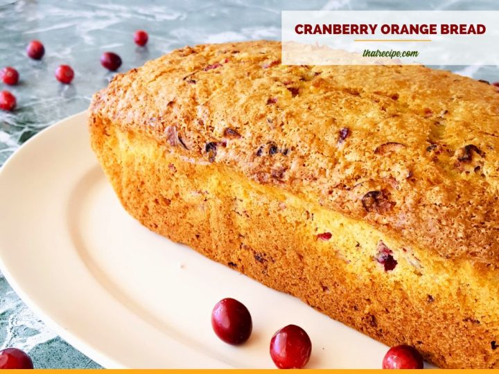 loaf of quick bread on a plate surrounded by cranberries with text overlay "Cranberry whole orange bread"