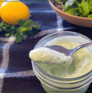 preserved lemon and herb salad dressing in a jar with a plate of salad