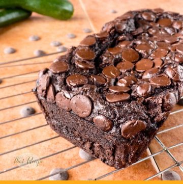 chocolate zucchini bread on a rack with fresh zucchini and chocolate chips