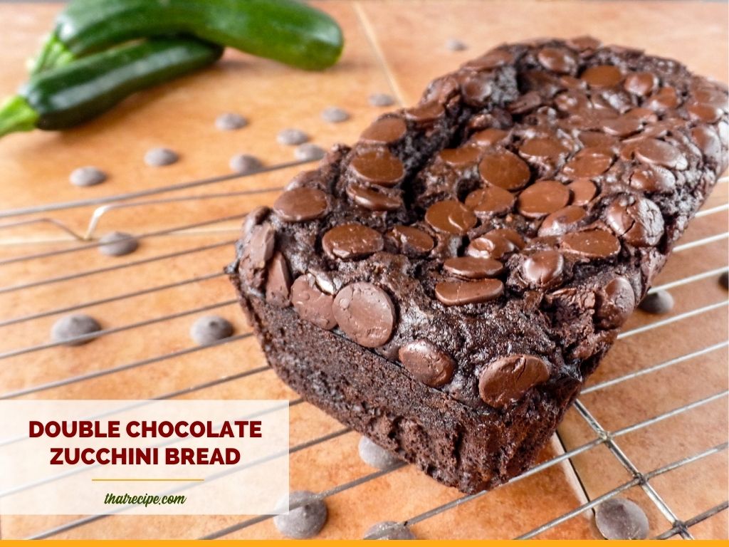 chocolate zucchini bread on a rack with fresh zucchini and chocolate chips