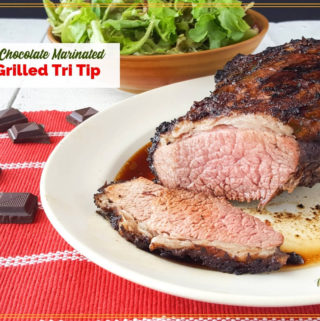 tri tip roast on a plate with a salad and chocolate pieces and text overlay "Spiced Chocolate Marinated Grilled Tri Tip"
