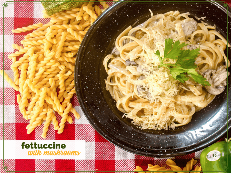 fettucine and mushrooms on a black plate on a red and white checked table cloth.