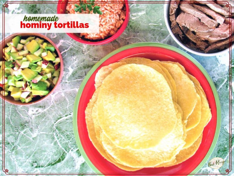 plate of hominy tortillas on a table with avocado salsa, Mexican rice and steak strips.