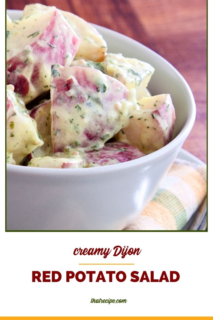 bowl of red potato salad on a table with text overlay "Creamy Dijon Potato Salad"