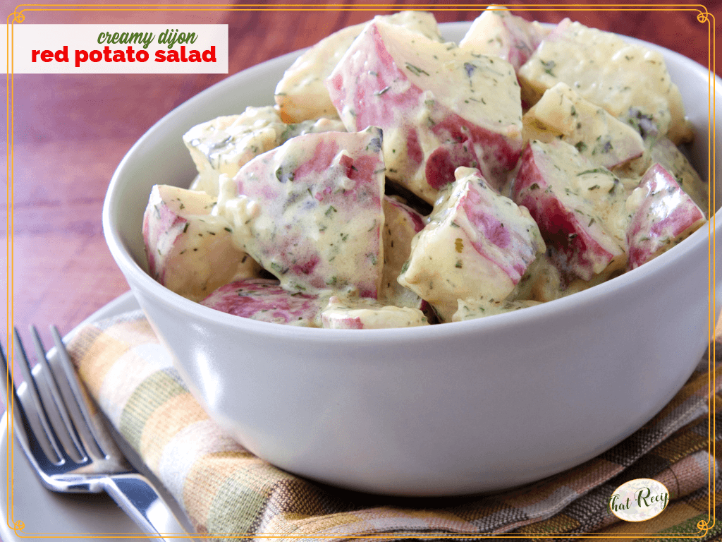 bowl of red potato salad on a table with text overlay "Creamy Dijon Potato Salad"