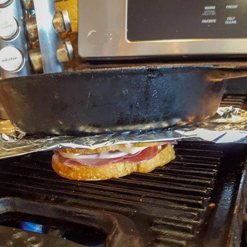 sandwich on griddle with cast iron skillet on top