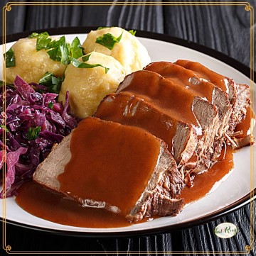 sliced sauerbraten on a plate with gravy, potatoes and red cabbage