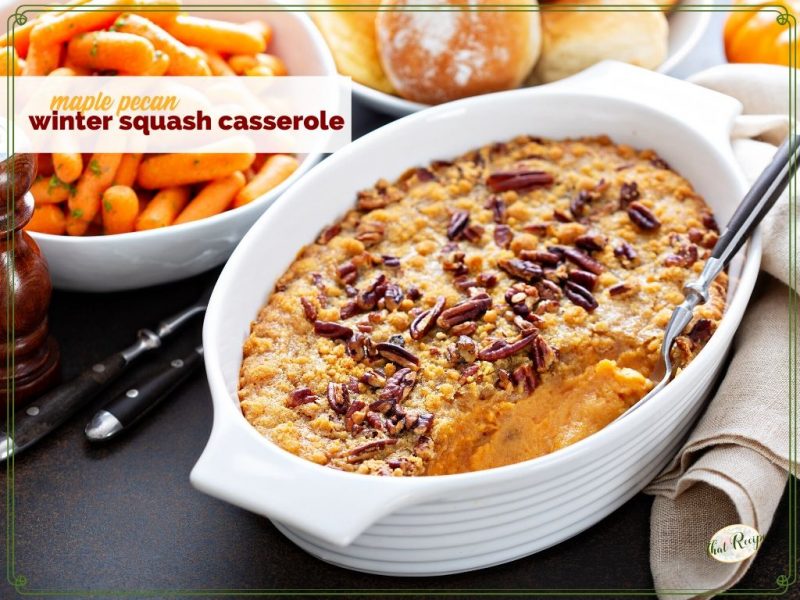 squash casserole on a table with carrots and rolls.