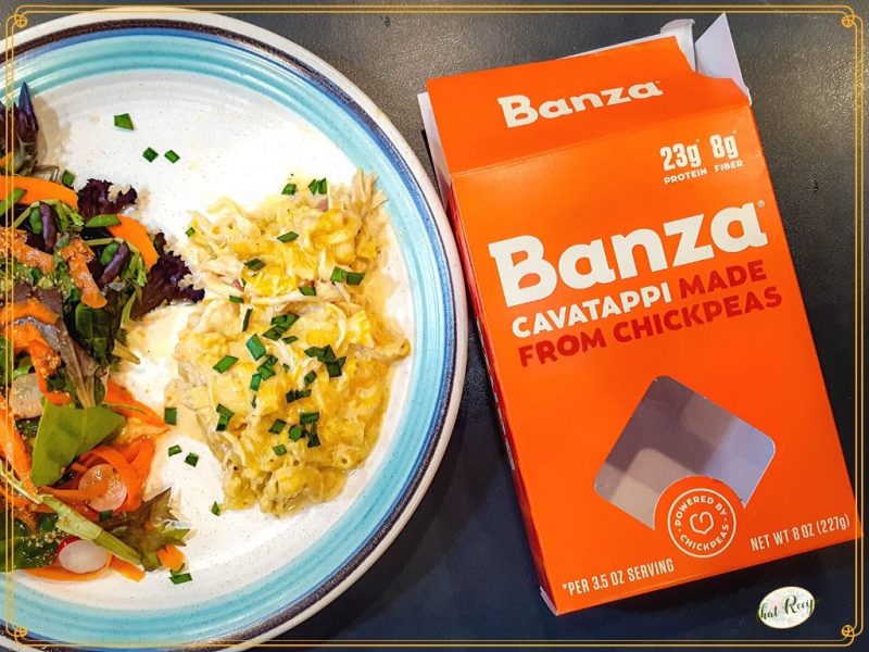 cheese pasta bake on a plate with a salad with a box of Banza pasta