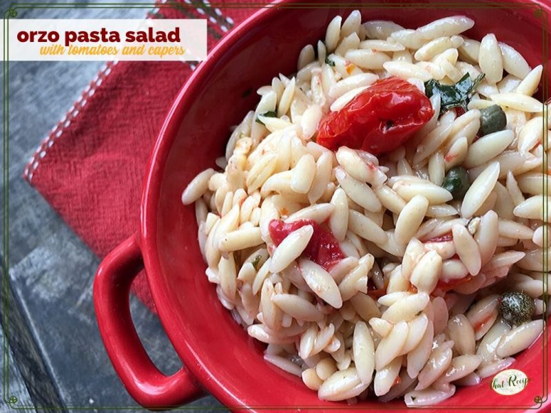 orzo pasta salad in a red bowl on blue slate with text overlay "orzo pasta salad with tomatoes and capers"