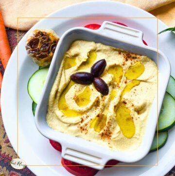 hummus in a bowl with roasted garlic head and vegetables