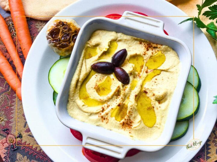 hummus in a bowl with roasted garlic head and vegetables