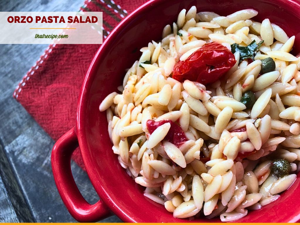 orzo pasta salad in a red bowl on blue slate with text overlay "orzo pasta salad with tomatoes and capers"