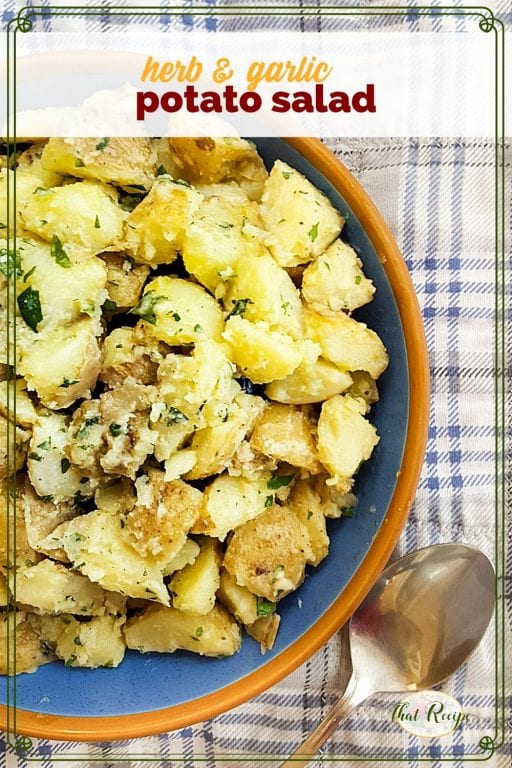 top down view of potato salad on a picnic blanket with text overlay "herb and garlic potato salad"