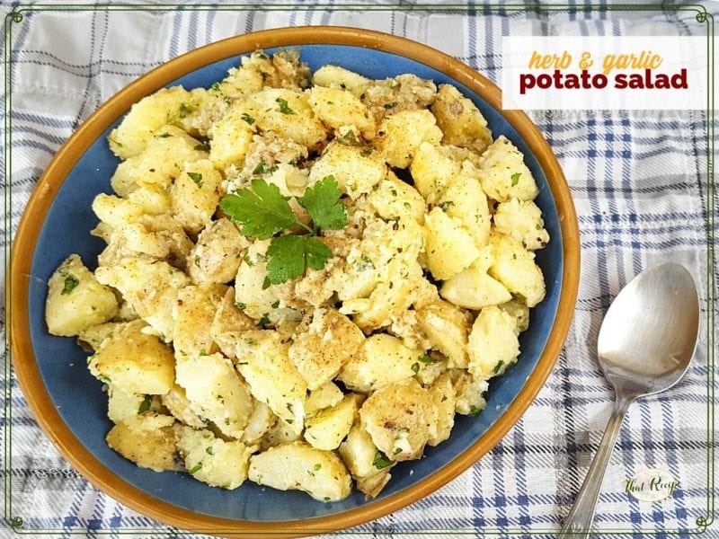 top down view of potato salad on a picnic blanket with text overlay "herb and garlic potato salad"