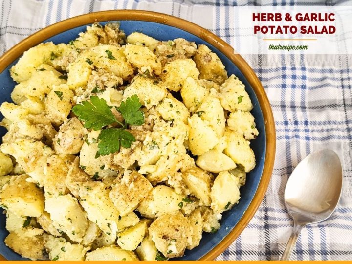 top down view of potato salad on a picnic blanket with text overlay "herb and garlic potato salad"