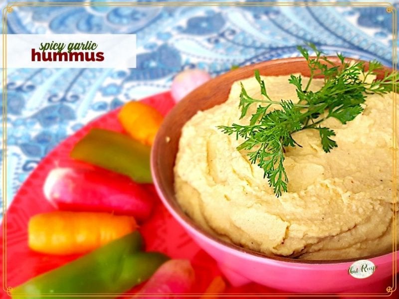 bowl of humus with vegetables around it on a plate and text overlay "spicy garlic hummmus"
