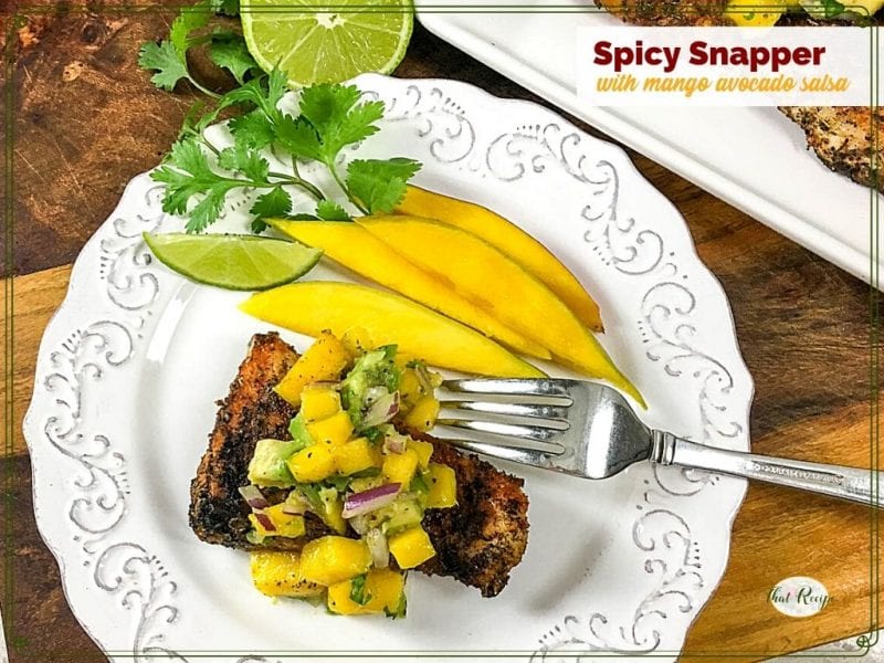cajun snapper on a plate topped with mango salsa and text overlay "spicy snapper with mango avocado salsa"