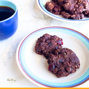 two chocolate cookies on a plate with a cup of coffee next to it and text overlay "Chocolate cranberry breakfast cookies"