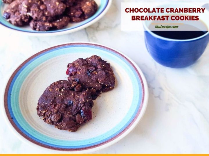 two chocolate cookies on a plate with a cup of coffee next to it and text overlay "Chocolate cranberry breakfast cookies"