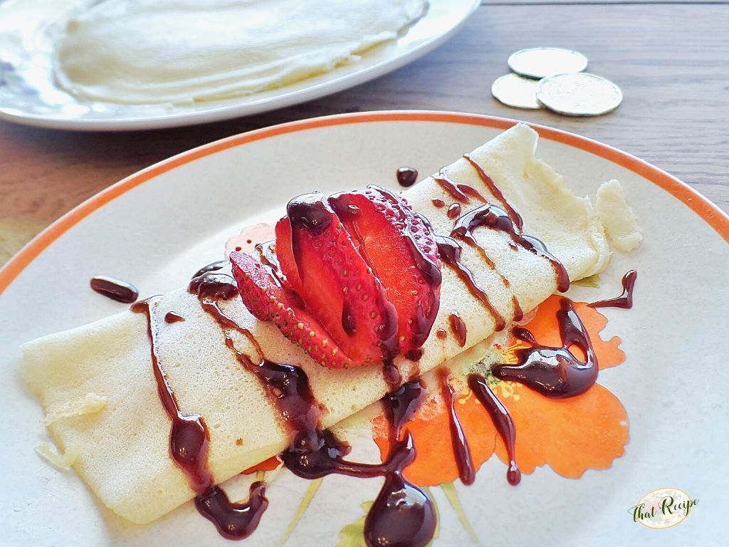 crepe topped with strawberry slices and chocolate drizzle