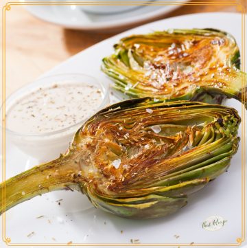 artichoke halves on a plate with dipping sauce