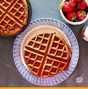 waffles on a plate and on a waffle iron with strawberries and whipped cream
